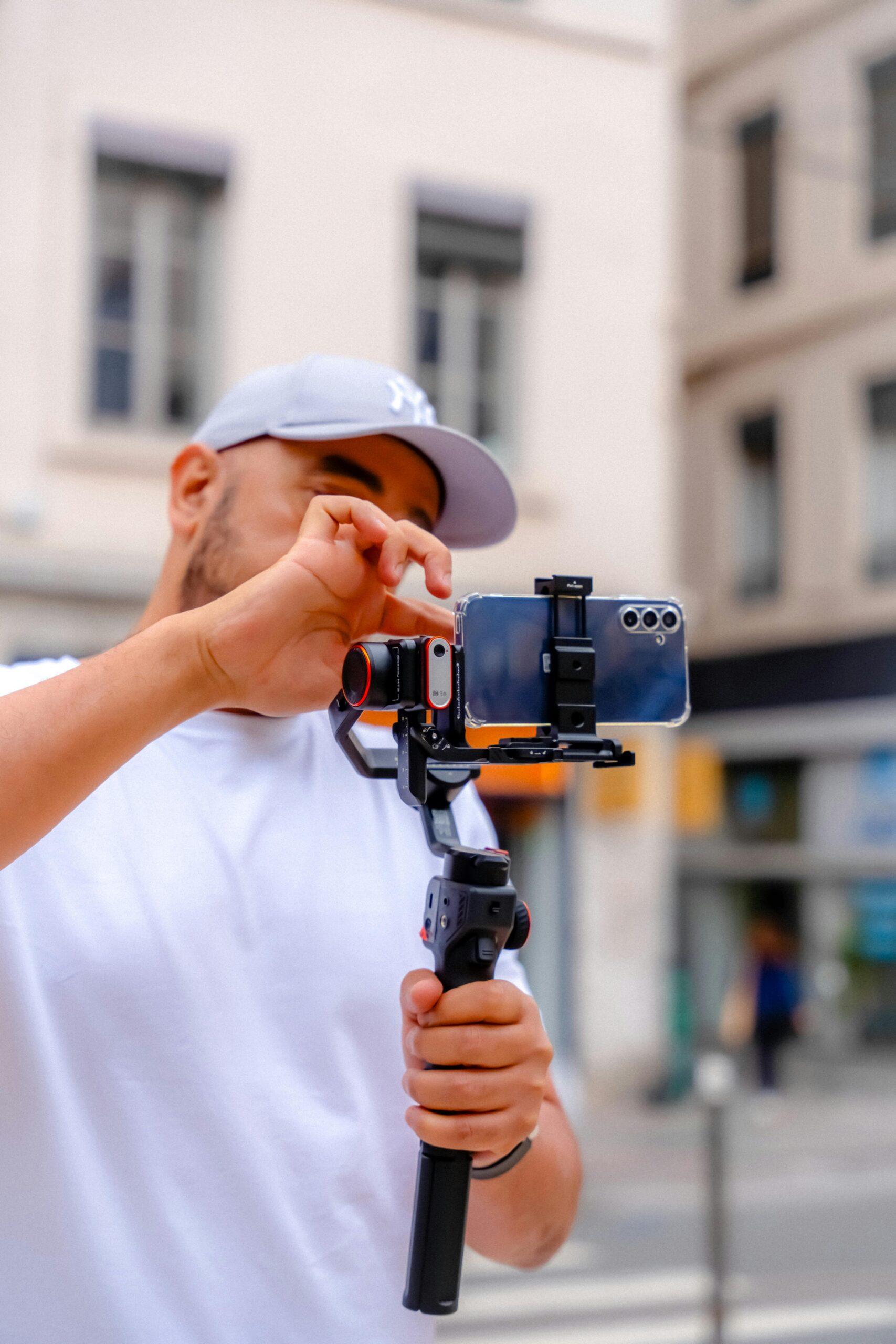 A man using a smartphone and stabilizer in an urban environment for filming.