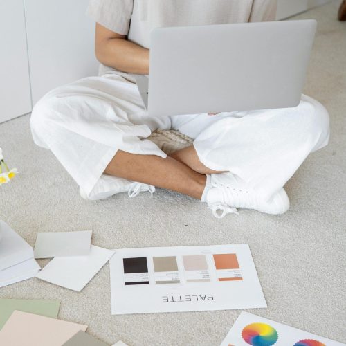 Young woman reviews color palettes for design project on laptop, sitting indoors.